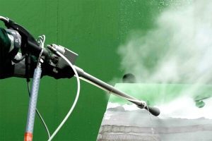 close up of high pressure water gun removing green paint from metal